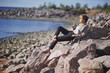 © raisondtre - Portrait young dreamy girl with closed eyes in a stylish coat and slacks sitting barefoot the rocks under rays of autumn sun on Bay.