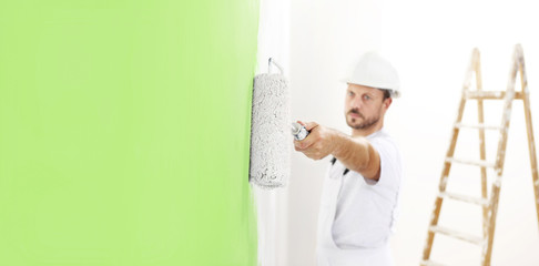 Wall Mural - painter man at work with a paint roller, wall painting green color ecological concept, web banner template