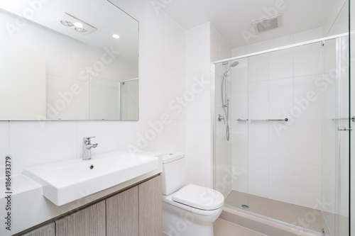 Plakat Nowoczesna minimalistyczna łazienka z drewnianymi szafkami i szklanym parawanem prysznicowym.