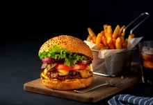 Tasty Grilled Beef Burger With Lettuce, Cheese And Onion Served On Cutting Board On A Black Wooden Table, With Copyspace.