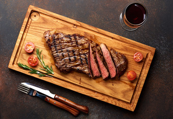 Grilled Black Angus Steak and a glass of red wine with tomatoes, rosemary on meat cutting board.