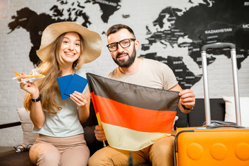 Wall Mural - Young couple sitting with german flag and passports at the travel agency office on the world map background prepairing for a trip to Germany