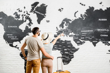 Young couple of travelers standing back near the big world map on the background choosing a place for a summer vacation