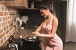 © LIGHTFIELD STUDIOS - beautiful smiling young woman in apron cooking with frying pan in kitchen