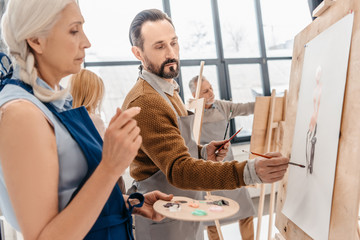 Wall Mural - male and female adult students painting together at art class