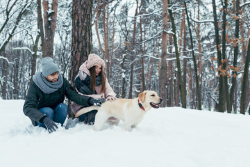 young couple having fun together with dog in winter park