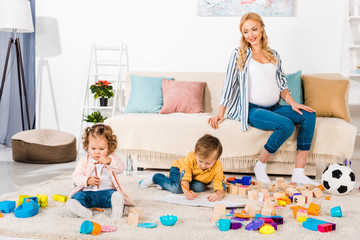 smiling pregnant woman looking how children playing on floor
