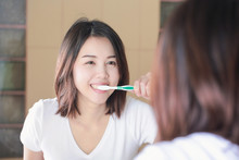 Young Woman Brushing Her Teeth At Mirror. After Awakening