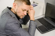 © Oleg - tired man with closed eyes and head leaning against hands at table with laptop in office