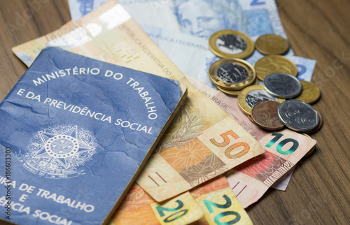 Fotografía Notas de dinheiro acompanhado de moedas, carteira de trabalho, lupa, calculadora