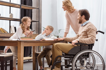 smiling father on wheelchair and mother teaching children at home