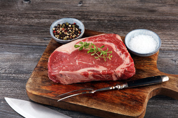 Wall Mural - Raw fresh meat Ribeye Steak, seasoning and meat fork on dark background