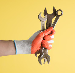 Handyman hand with glove holding wrenchs on yellow background