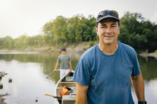 Portrait Of Mid Adult Man Pushing Boat With Friend Towards Lakeshore