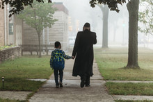 Rear View Of Father And Boy Walking On Footpath During Foggy Weather