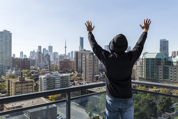 Man on a high rise building balcony overlooking the city, with hands outstretched. Expressing his joy of life.