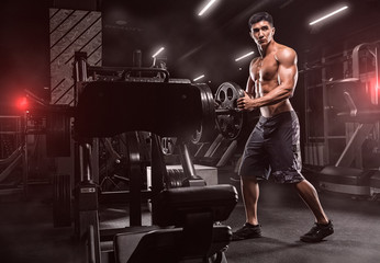 A young handsome, inflated man, equips a machine for exercise. Training for the feet, on a beautiful background, in a modern sports club.