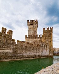 Scaliger castle is historical landmark of the city Sirmione in Italy on the lake Garda. Medieval Italian castle. The stone walls of an ancient tower on the background of cloudy sky.