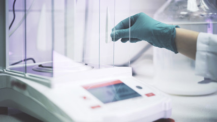scientist s hand in a green glove is putting liquid at electronic scales in a lab. medium shot. uni 