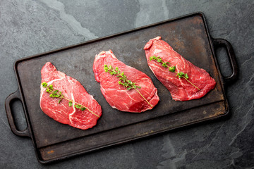 Wall Mural - Raw beef steaks with herbs and spices on cast iron frying board, top view