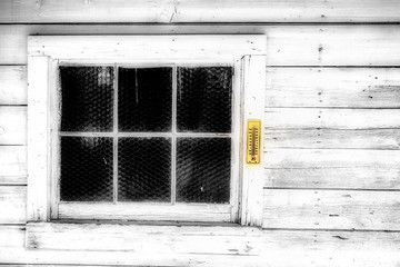 An old weather thermometer hanging on an old six paned exterior window in a wide planked timber wall