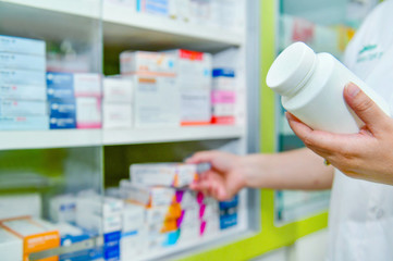 Wall Mural - Pharmacist holding bottle of medicine and capsule pack in pharmacy drugstore.