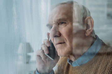 Wall Mural - Behind the glass view of senior disturbed man making a phone call