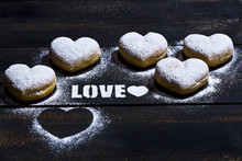 The Word 'Love' Stenciled With Icing Sugar And Five Heart-shaped Crullers On Dark Wood