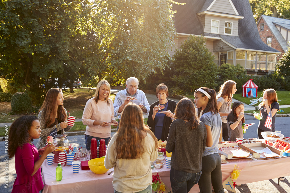 Neighbours talk and eat around a table at a block party - obrazy, fototapety, plakaty 
