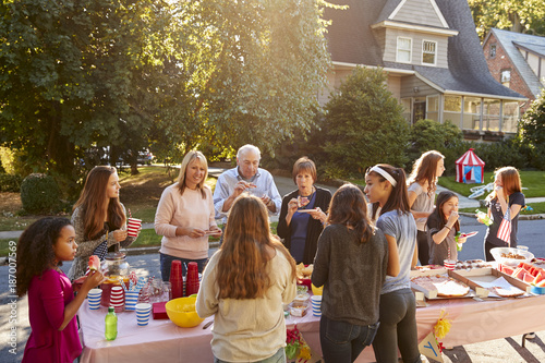 Fotografía Neighbours talk and eat around a table at a block party