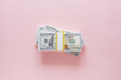 © Kristin Duvall/Stocksy - Overhead view of stack of 100 dollar bills on pink background