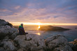 © Leander Nardin/Stocksy - young man sitting on the edge of a cliff enjoying beautiful suns