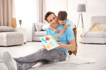 Wall Mural - Young man with greeting card for Father's Day from his little son at home