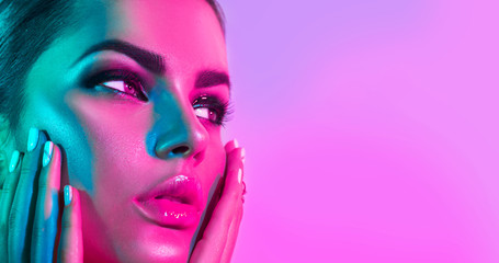 Wall Mural - Fashion model woman in colorful bright lights with trendy makeup and manicure posing in studio over purple background