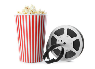 Wall Mural - Paper cup with tasty popcorn and movie reel on white background