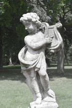 Figure Of Cute Little Cupid Or Boy Playing Harp As A Symbol Of Love, Kindness, And Suffering, Sweet Cherub On A Pedestal.