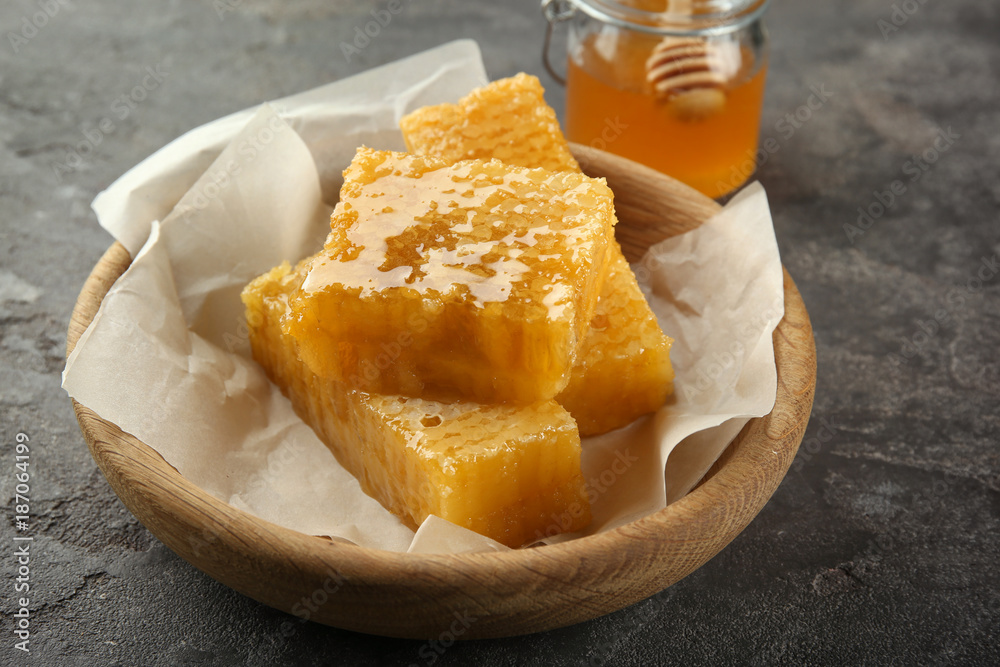 Bowl with sweet honeycombs on grey background
