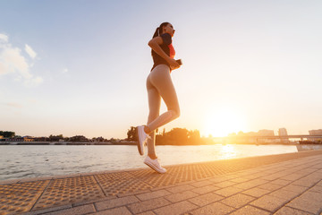 girl on a sunset background performs an evening run with a phone in her hands view from below