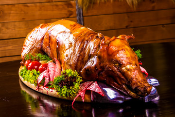 Roasted piglet decorated with vegetables and ham on platter