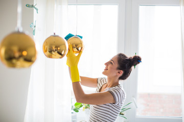 Side view of the young woman in yellow gloves who holding rag and wiping the decorative balls in the room