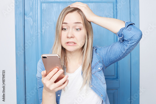 Fotografie, Obraz Annoyed attractive female gestures with irritation, frowns face as receives unpleasant message, clenches teeth, looks at camera, isolated over white background