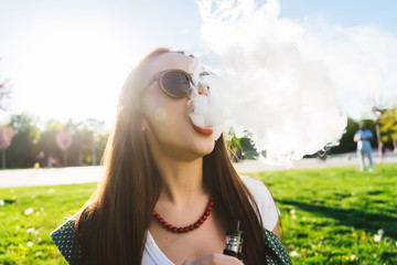 Happy fashion smiling Woman in sunglasses smoking vape on street,smoke