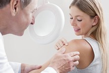 Doctor Examining Mole On Young Woman's Shoulder