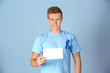 © Africa Studio - Young man in t-shirt with blue ribbon holding blank card on color background. Prostate cancer awareness concept