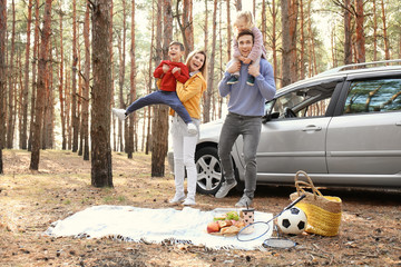 Poster - Young couple playing with their children on picnic in pine forest