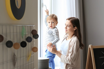 Poster - Beautiful young woman with her baby near window at home