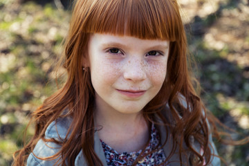 Close-up of a happy red-haired little girl outdoors