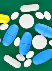 Assorted pharmaceutical medicine pills, tablets and capsules on green background