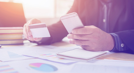 Man holding business card and dialing number at wooden desk,verifies account balance on mobile banking application.Online payment shopping,selective focus,vintage color