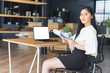 © kenchiro168 - Young business woman reading a report sitting in a coffee shop and working on blank screen laptop.
